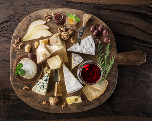 Cheese platter with organic cheeses, fruits, nuts and wine on wooden background. Top view. Tasty cheese starter.