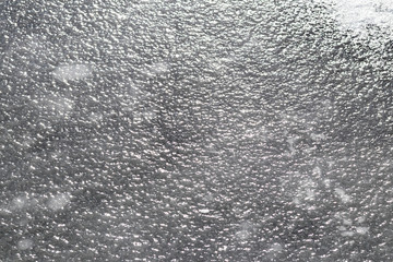 the lake has frozen ice on it is uneven. has sharahovatast. shade of gray. there is a crack on it