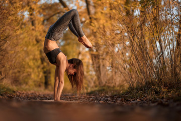 Young woman practicing yoga exercise at autumn park with yellow leaves. Sports and recreation lifestyle