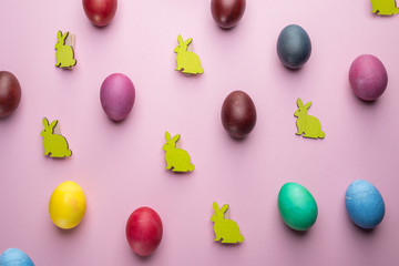 Colorful Easter eggs and wooden Easter Bunnies as attribute of Easter celebration. Pink background.