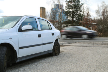 A car destroyed during the traffic accident. The car is abandoned and stands by the road. It is passed by other cars. 