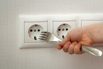 Child sticks the fork into an electrical outlet. Dangerous situation at home.