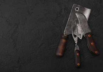 Vintage meat knife and fork and hatchet on black table background. Butcher utensils. Space for text