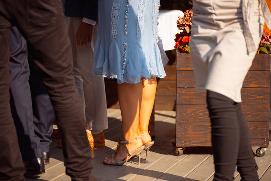 slender female legs in a blue skirt and beige heeled shoes surrounded by male legs on a wooden floor. Party festive day at the wedding