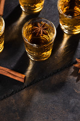 Shoot glass of alcoholic drinks with star anise and cinamon on metal table and black stone tray. 