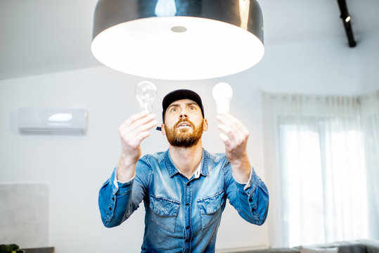 Handyman choosing between energy save and cheap incandescent lamp while changing light in the appartment