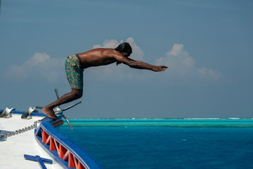 maldivian man diving from boat in blue ocean