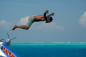 maldivian man diving from boat in blue ocean