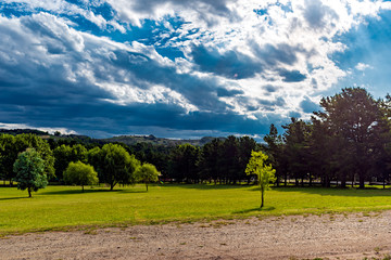 Landscape with mountains on the back, a lot of trees, green grass and a road in the front on a cloudy day with sunrays on the image