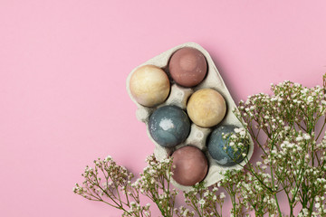 Selective focus of coloured decorated easter eggs in cardboard container, gypsophila flowers