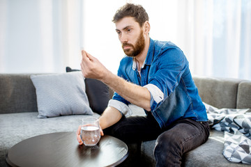 Man drinking some medicines feeling bad or having hangover after the alcohol party, sitting on the couch at home