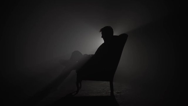 Silhouette of man in suit sitting in armchair and smoking cigarette