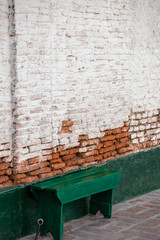 Green bench next to an old bricks wall