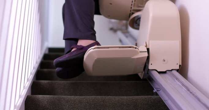 Senior Woman Sitting On Stair Lift At Home To Help Mobility