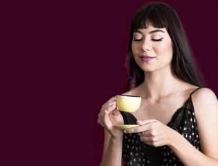 Beautiful Young Woman Holding a Yellow Cup of Coffee Isolated on a Horizontal Purple Backdrop