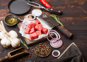 Raw lean diced casserole beef pork steak with vintage meat hatchet and fork on wooden background. Salt and pepper with fresh rosemary, red onion and garlic with rosemary.