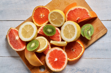 Sliced lemons, oranges, grapefruits and kiwi on a wooden plate.