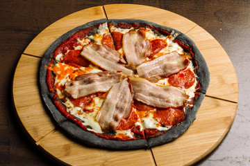 Pepperoni pizza with ham and sausages on black pastry.