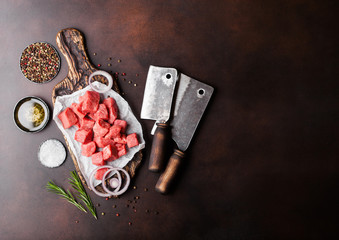Raw lean diced casserole beef pork steak on chopping board with vintage meat hatchets on brown background. Salt and pepper with fresh rosemary.Space for text
