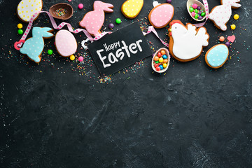 Obraz na płótnie Canvas Easter greeting card. Happy Easter. Easter gingerbread cookies and decorative colored eggs. On a black background. Top view. Free copy space.