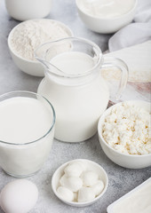 Fresh dairy products on white table background. Jar and glass of milk, bowl of sour cream, cottage cheese and baking flour and mozzarella. Eggs and cheese.