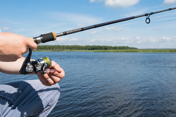 hands holding spinning for catching fish against the blue sky and white clouds