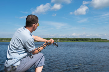 a fisherman on the bank fishes on a spinning on the river against the blue sky