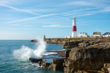Waves break against the rocky coastline of Portland Bill with the lighthouse and visitor centre in the background