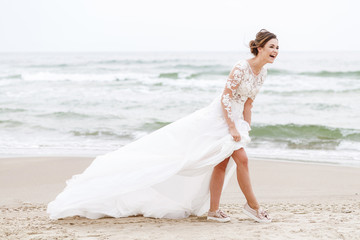 Fototapeta na wymiar positive bride runs on the sea beach on an overcast day