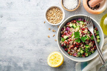 Healthy pearl barley salad with beans, cucumbers, red onion, sunflower seeds, pomegranate and parsley in bowl on concrete background. Top view. Copy space.