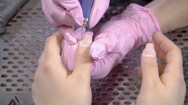 close uo top view manicurist in pink rubber gloves remove cuticles from costumers finger using electric file nail drill. macro