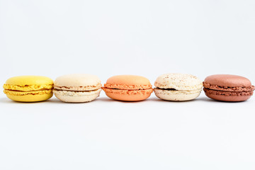 Side view of a line of five sweet French macarons isolated on white, flavours of lemon, caramel, vanilla, coconut and chocolate