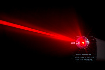 Red laser beam from a lab laser. Warning notice on front. Black background. Beam scatters near aperture. - obrazy, fototapety, plakaty