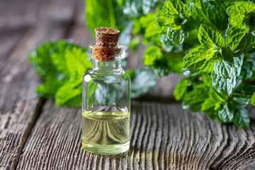 A bottle of peppermint essential oil with fresh peppermint leaves