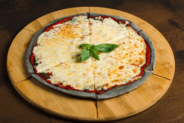 Cheese Pizza, black pastry on a wooden board. Decorated with greens.