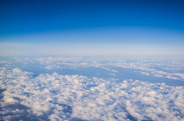 View from a plane window on clouds and blue clear sky and the earth from height. Beautiful view from air of mountains. 