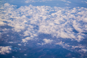 Fototapeta na wymiar View from a plane window on clouds and blue clear sky and the earth from height. Beautiful view from air of mountains. 