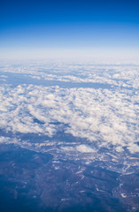 Obraz na płótnie Canvas View from a plane window on clouds and blue clear sky and the earth from height. Beautiful view from air of mountains. 