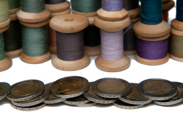 Rows of coins isolated on white background next to multicolored thread on wooden spool
