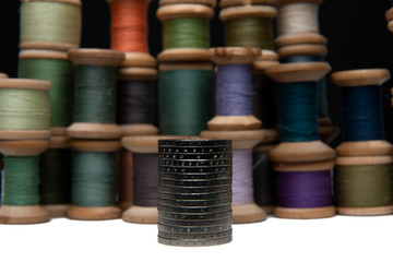 Rows of coins isolated on white background next to multicolored thread on wooden spool