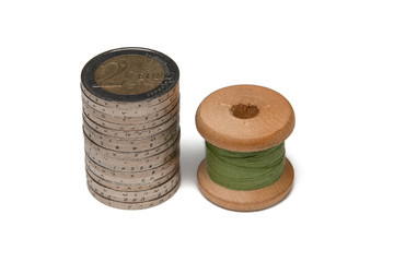 Rows of coins isolated on white background next to multicolored thread on wooden spool