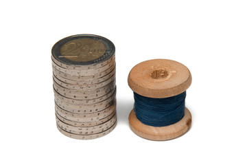 Rows of coins isolated on white background next to multicolored thread on wooden spool