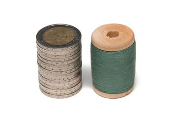 Rows of coins isolated on white background next to multicolored thread on wooden spool
