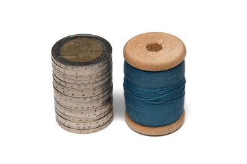 Rows of coins isolated on white background next to multicolored thread on wooden spool