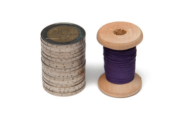 Rows of coins isolated on white background next to multicolored thread on wooden spool