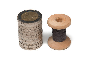 Rows of coins isolated on white background next to multicolored thread on wooden spool