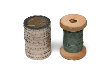 Rows of coins isolated on white background next to multicolored thread on wooden spool