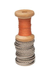 Rows of coins isolated on white background next to multicolored thread on wooden spool