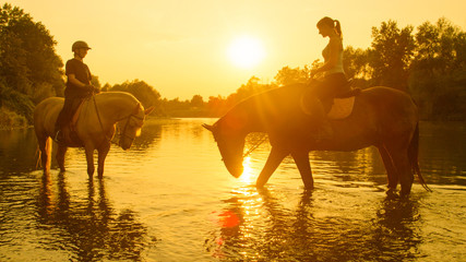 LENS FLARE: Happy girls riding their beautiful horses along the calm river.