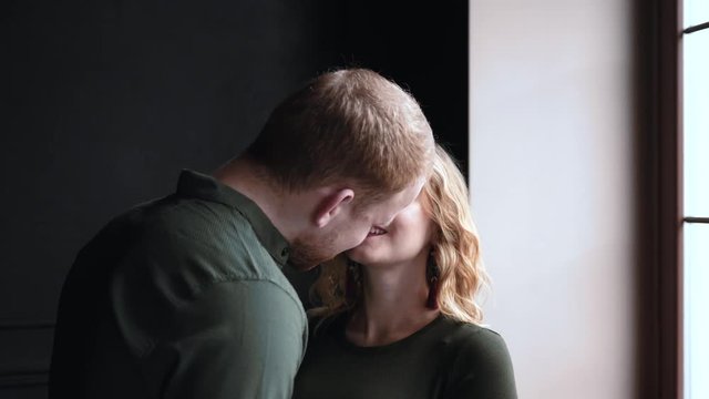 Pregnant family young husband and wife enjoy smile kissing by window
